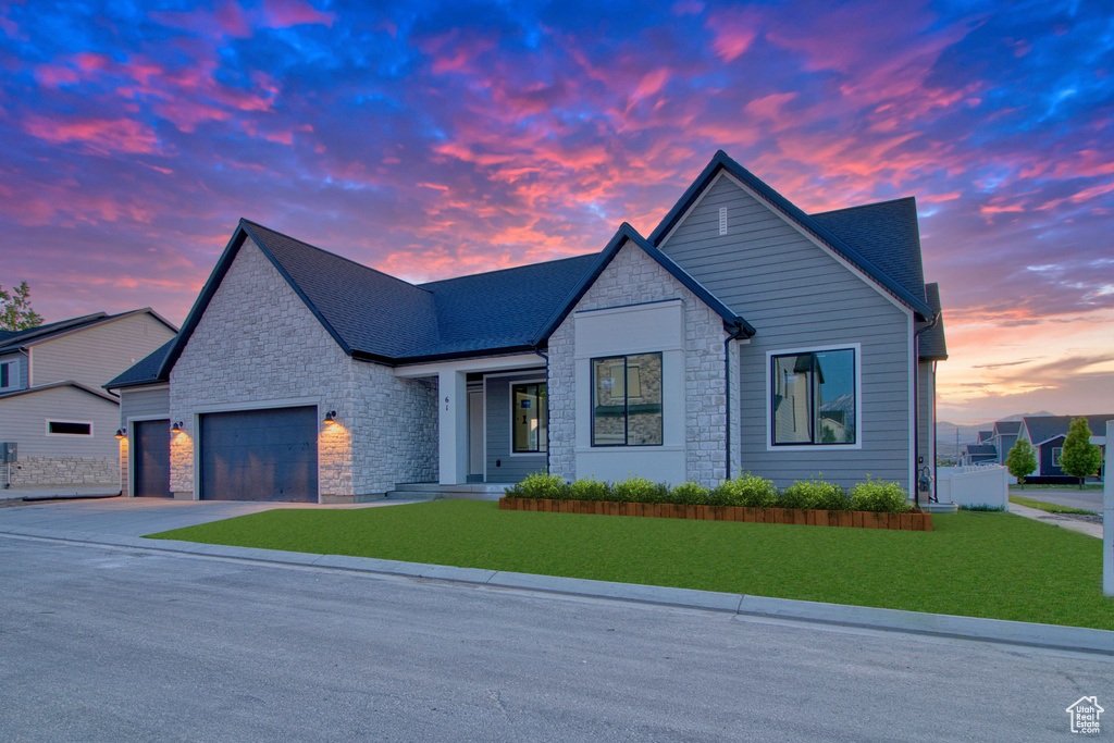 View of front of house with stone siding, a garage, a lawn, and driveway