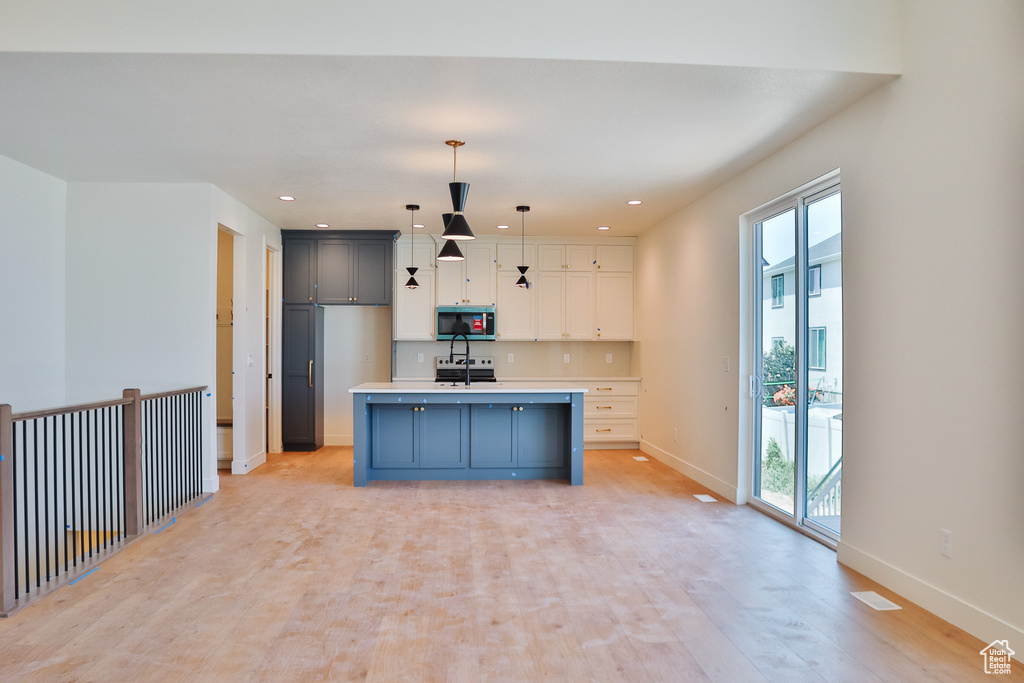 Kitchen featuring stainless steel microwave, baseboards, light countertops, pendant lighting, and a kitchen island with sink