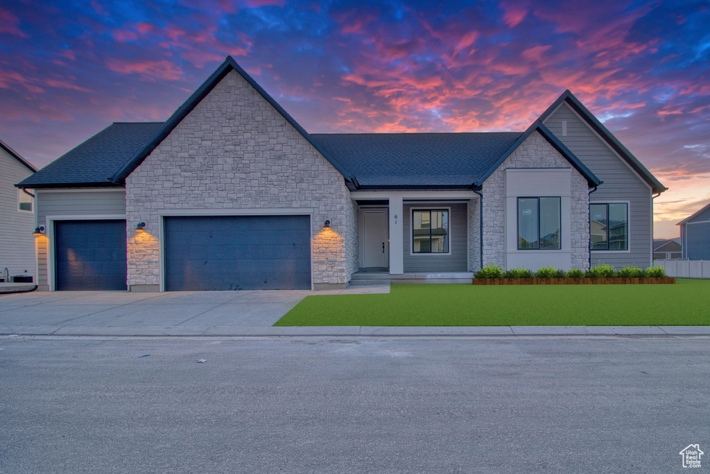 View of front of home featuring stone siding, an attached garage, concrete driveway, and a yard