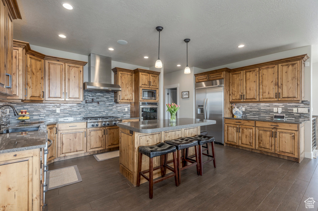 Kitchen with built in appliances, wall chimney exhaust hood, a sink, tasteful backsplash, and a kitchen island
