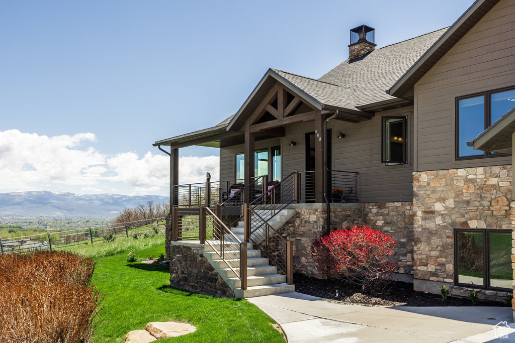 View of side of home with stone siding, a chimney, a shingled roof, stairway, and a porch