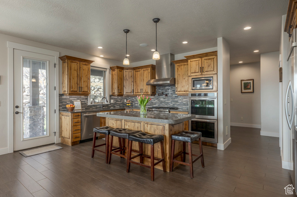 Kitchen with wall chimney range hood, appliances with stainless steel finishes, backsplash, baseboards, and recessed lighting