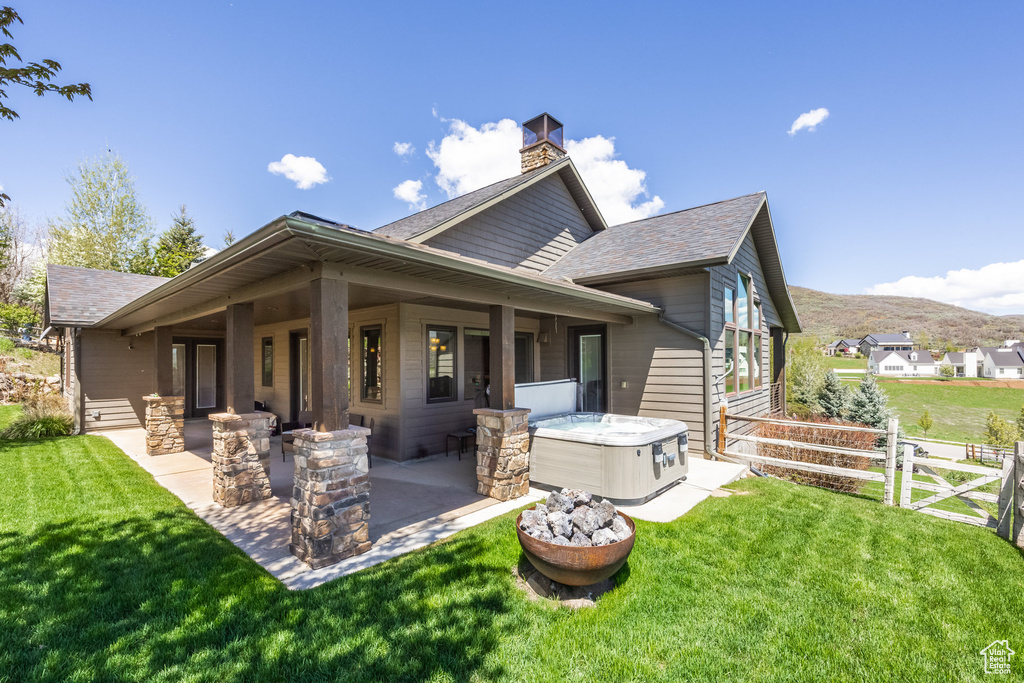 Rear view of house with a patio, roof with shingles, a chimney, a hot tub, and a mountain view