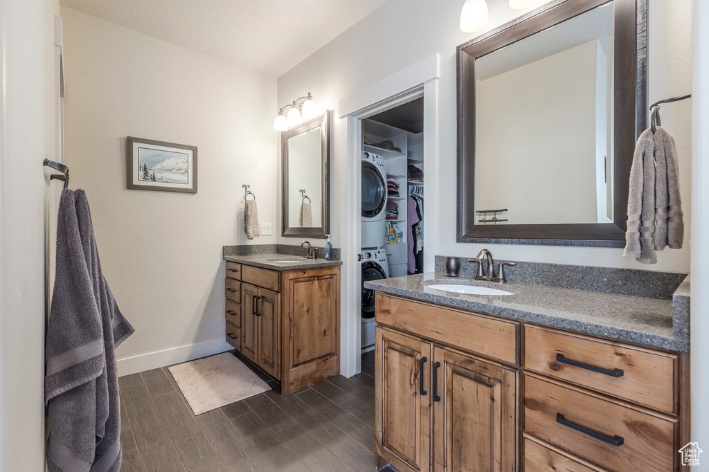 Bathroom featuring stacked washer / dryer, wood finished floors, baseboards, two vanities, and a walk in closet