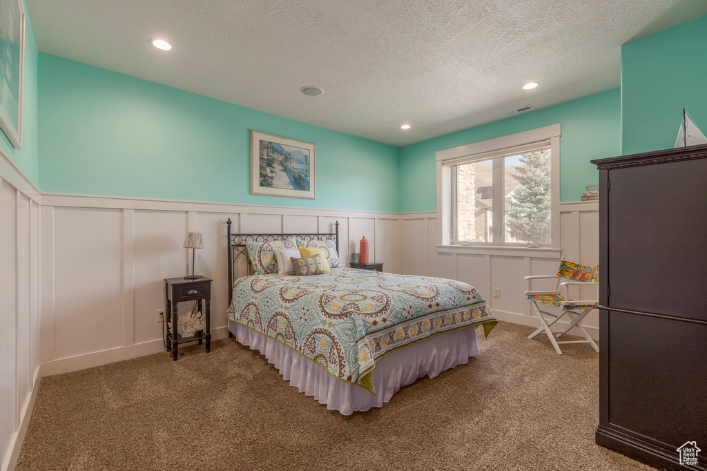 Bedroom with a decorative wall, wainscoting, carpet floors, recessed lighting, and a textured ceiling
