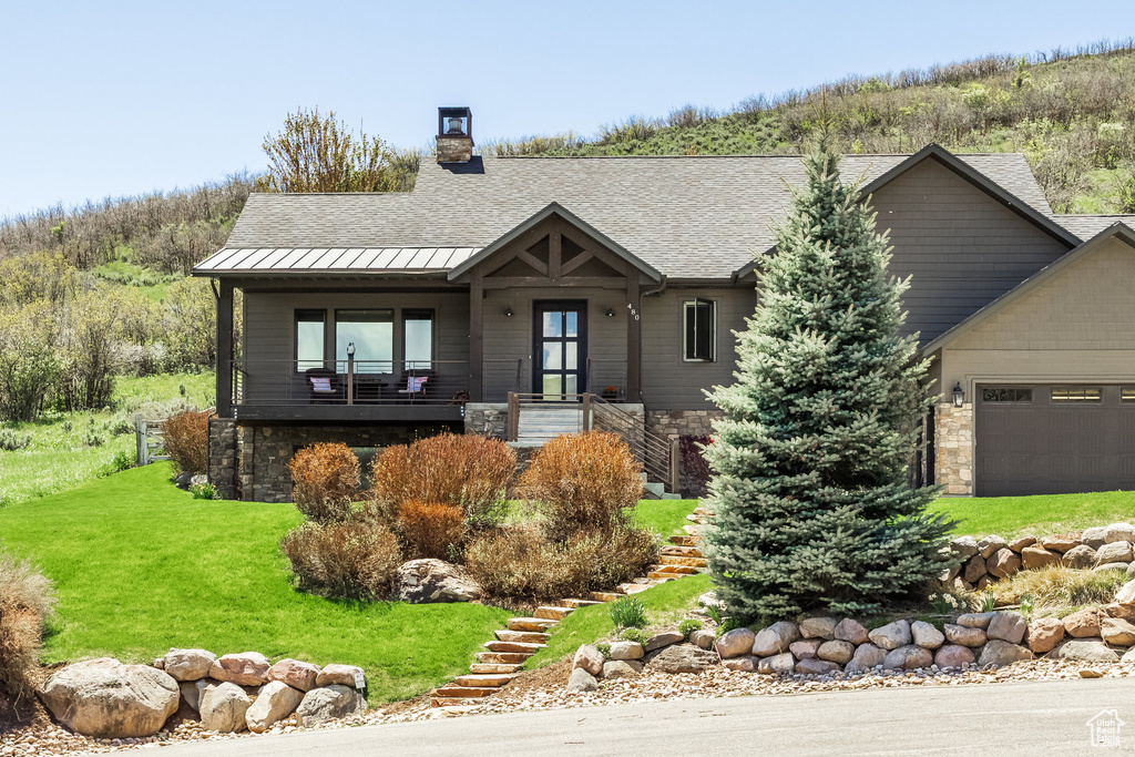 View of front facade featuring a standing seam roof, stairway, roof with shingles, a front lawn, and stone siding