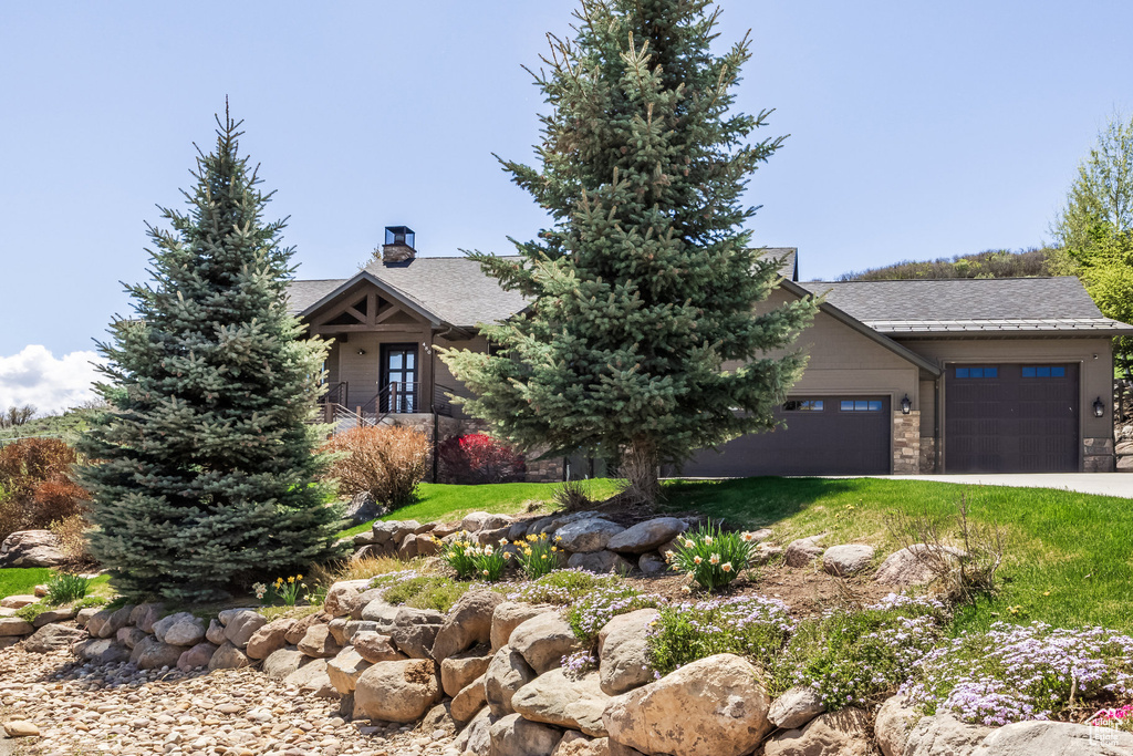 View of property hidden behind natural elements featuring a garage, a chimney, driveway, and a front yard