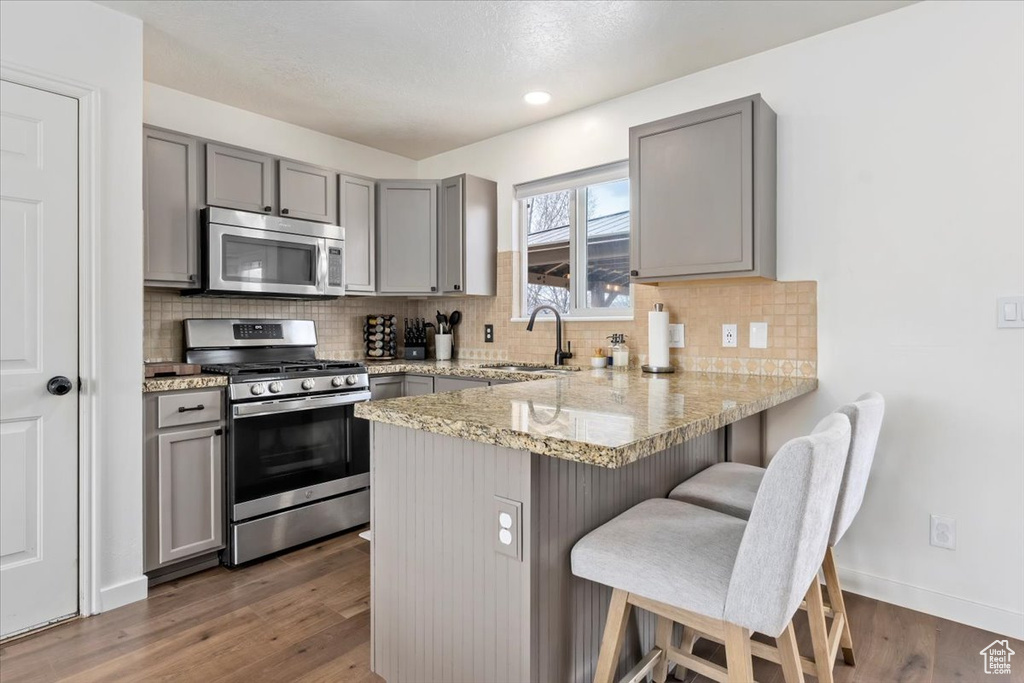 Kitchen with a sink, gray cabinets, stainless steel appliances, a kitchen bar, and a peninsula