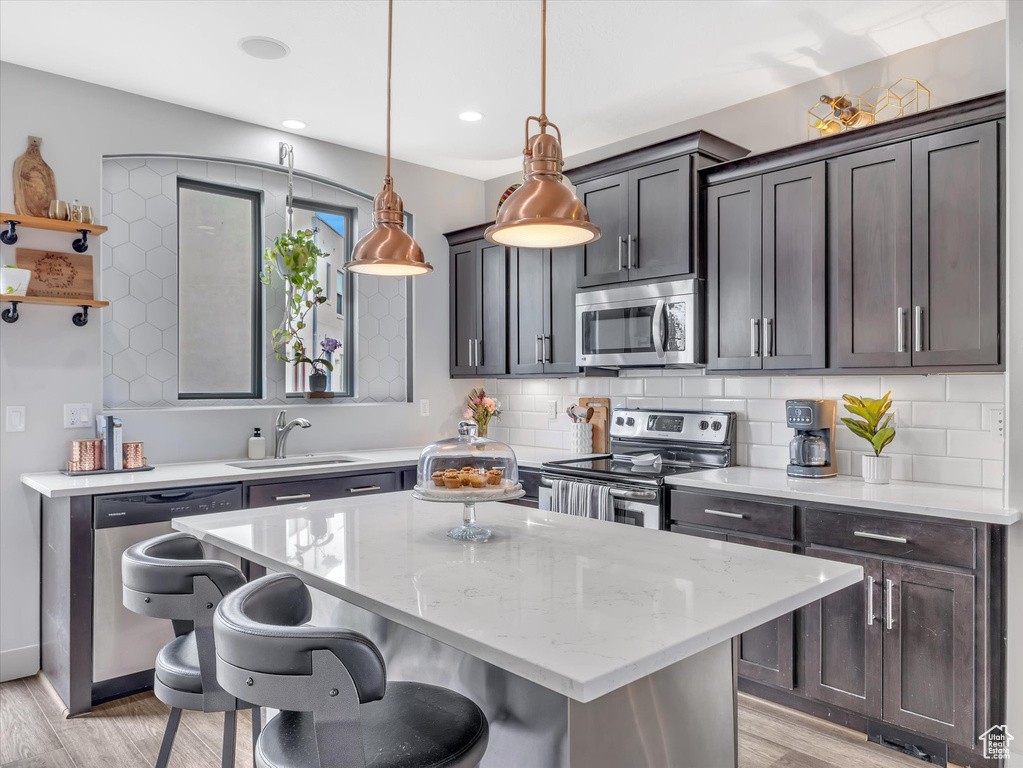 Kitchen featuring a breakfast bar, a sink, a kitchen island, light wood-style flooring, and appliances with stainless steel finishes