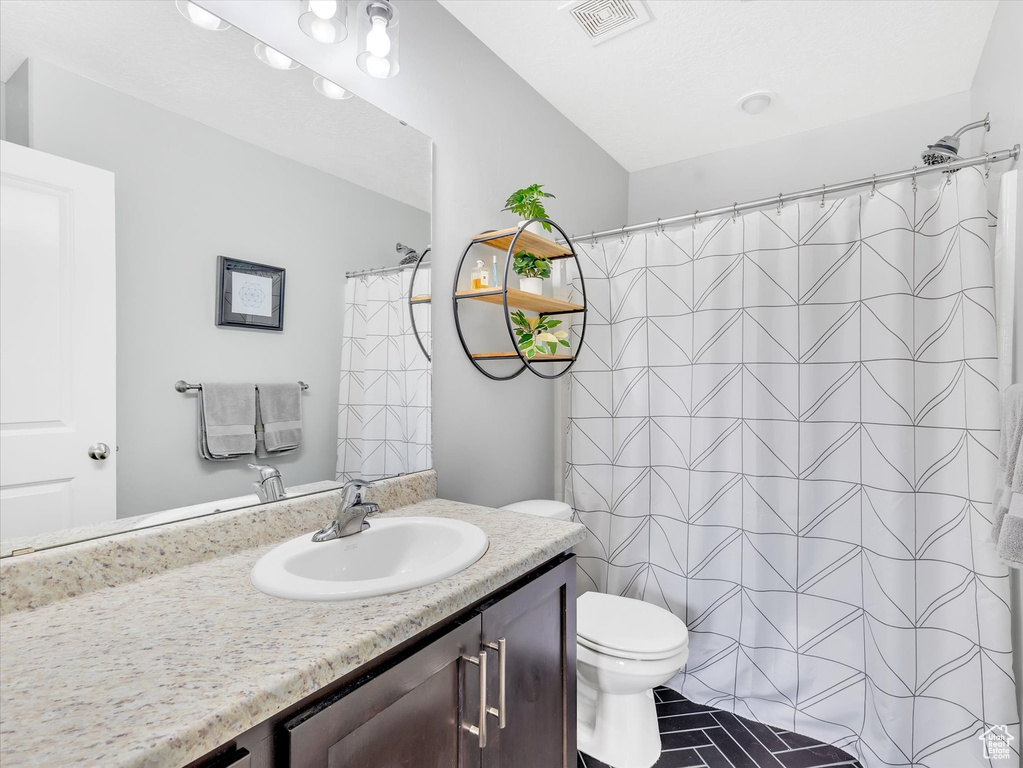Bathroom with toilet, a shower with curtain, vanity, and visible vents