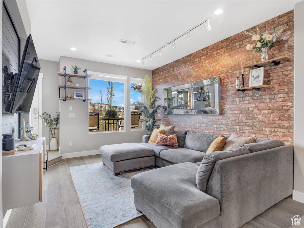 Living area with an accent wall, light wood-style floors, brick wall, baseboards, and recessed lighting