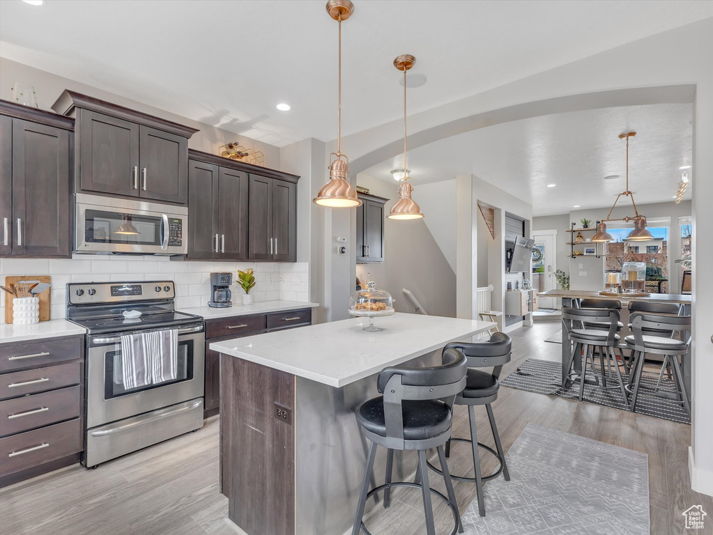 Kitchen featuring light countertops, a kitchen island, dark brown cabinetry, tasteful backsplash, and appliances with stainless steel finishes