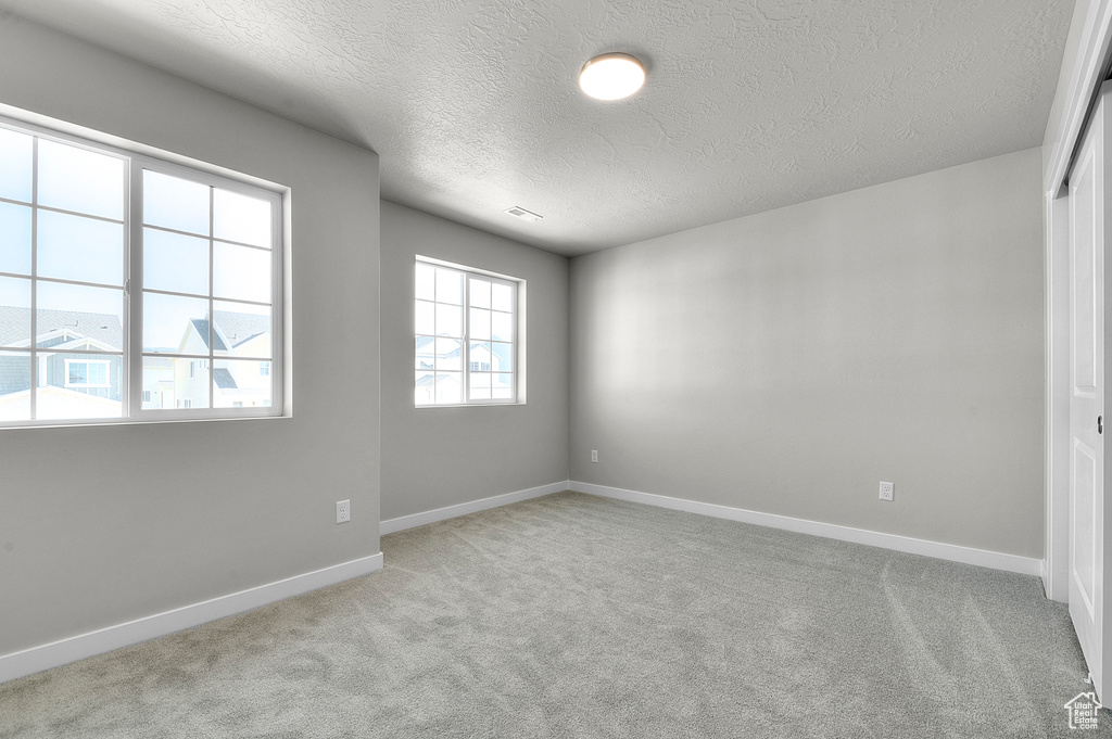Carpeted empty room featuring a textured ceiling and baseboards