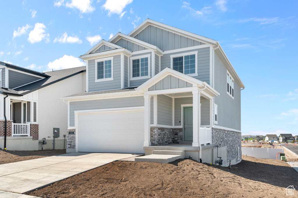 Craftsman house with board and batten siding, driveway, stone siding, and an attached garage