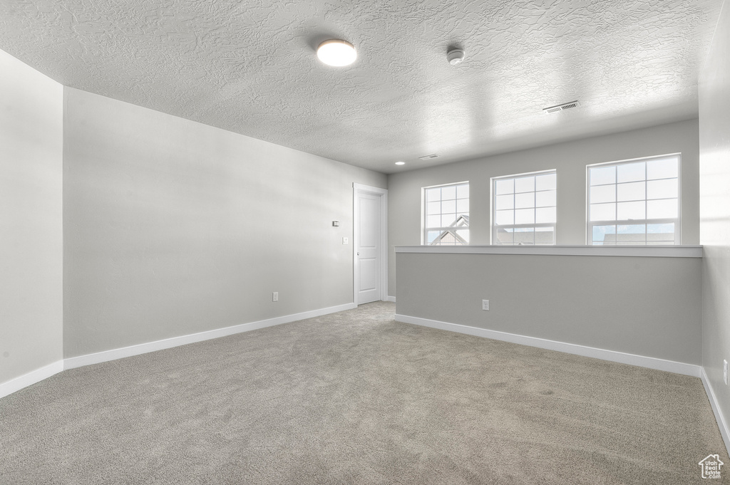 Spare room with a textured ceiling, carpet floors, baseboards, and a smoke detector