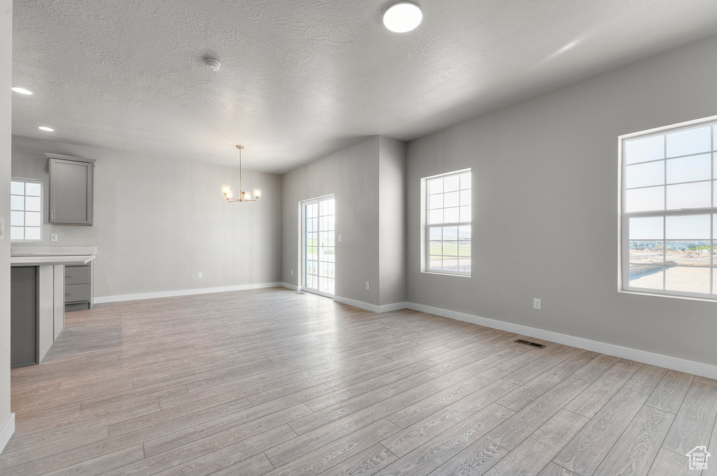 Unfurnished living room featuring a chandelier, light wood-style flooring, baseboards, a textured ceiling, and recessed lighting