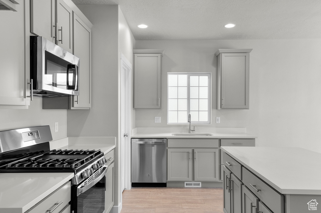 Kitchen featuring appliances with stainless steel finishes, a sink, gray cabinets, light wood-type flooring, and light countertops