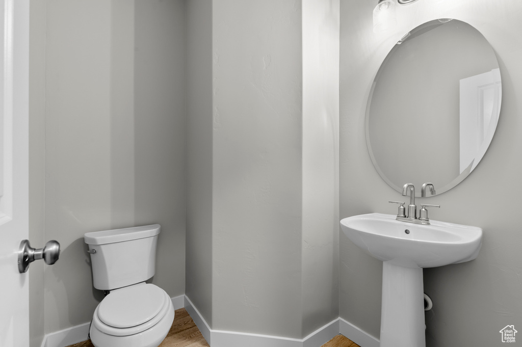 Half bathroom with toilet, wood finished floors, and baseboards