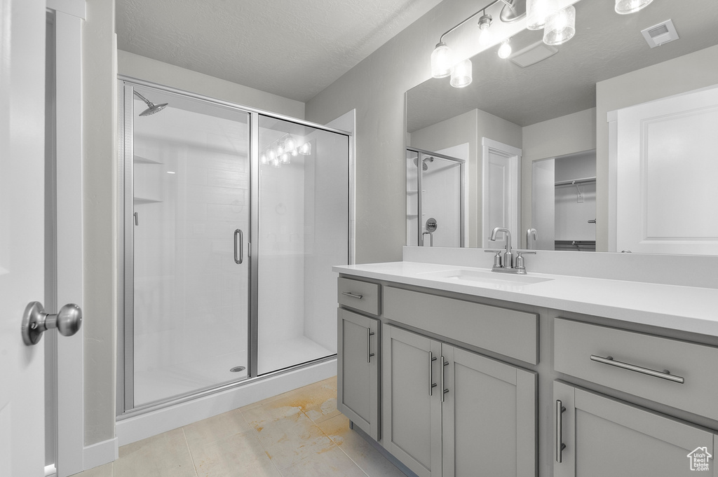 Full bath featuring a shower stall, vanity, a walk in closet, and a textured ceiling