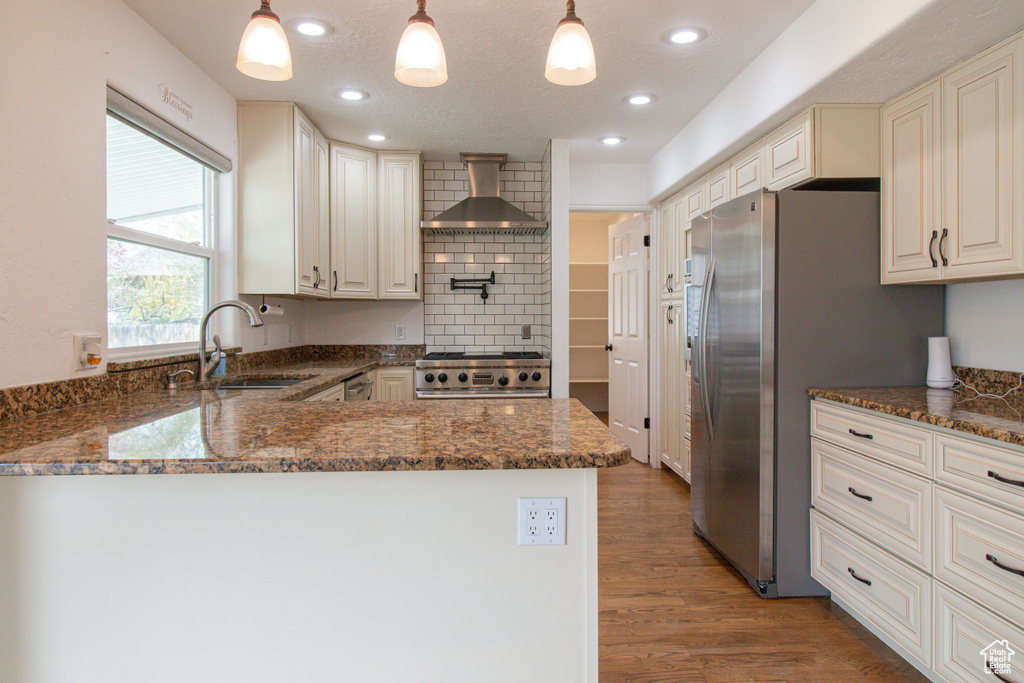 Kitchen featuring stove, a sink, wall chimney exhaust hood, dark stone counters, and a peninsula
