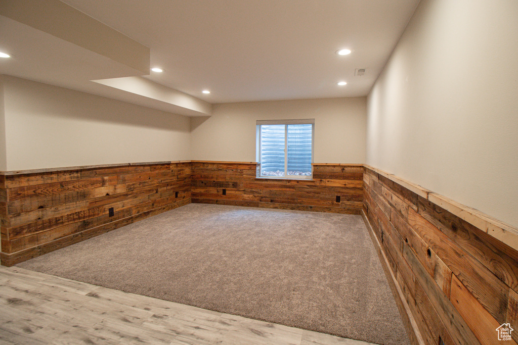 Basement with wood finished floors, a wainscoted wall, carpet, wood walls, and recessed lighting