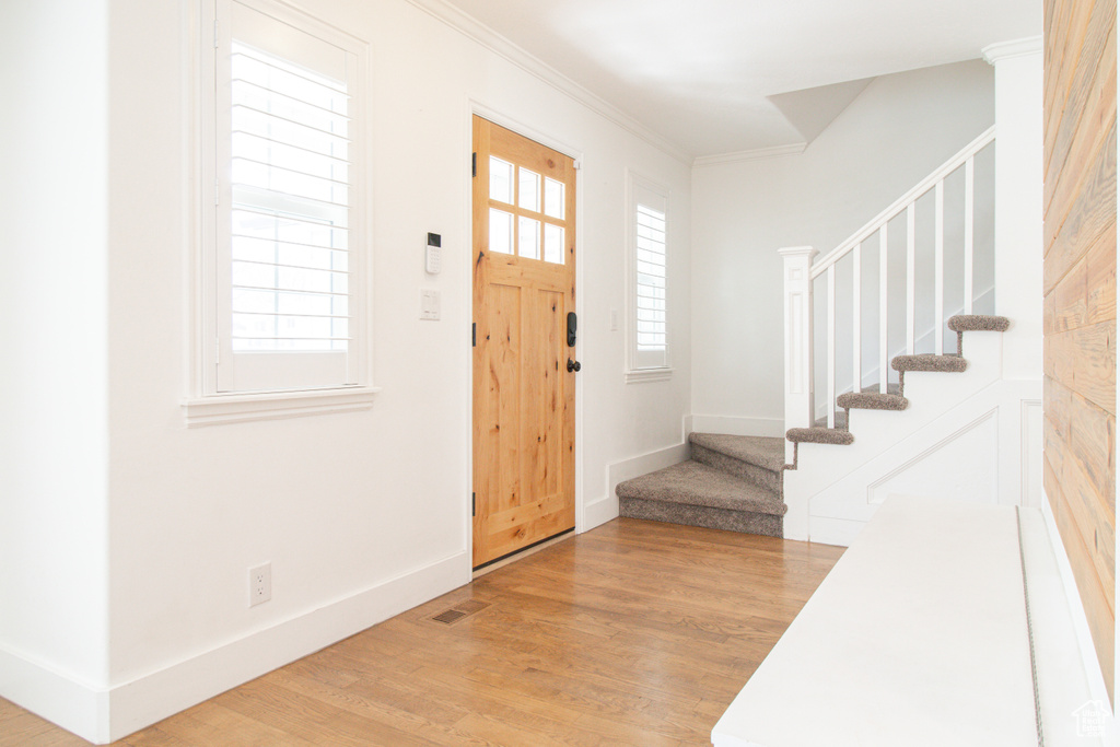 Entryway with stairway, crown molding, light wood-type flooring, baseboards, and visible vents