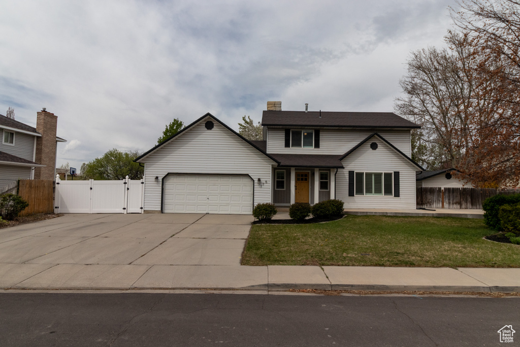 Traditional-style home with a front lawn, a gate, concrete driveway, fence, and an attached garage