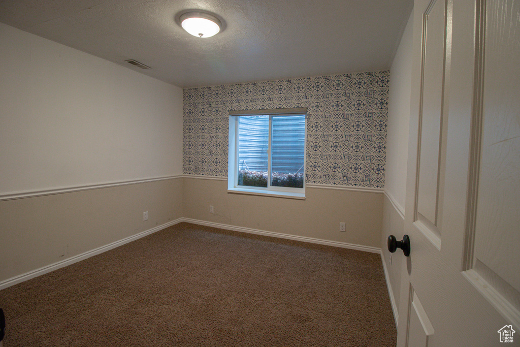 Empty room featuring baseboards, visible vents, dark colored carpet, and wallpapered walls