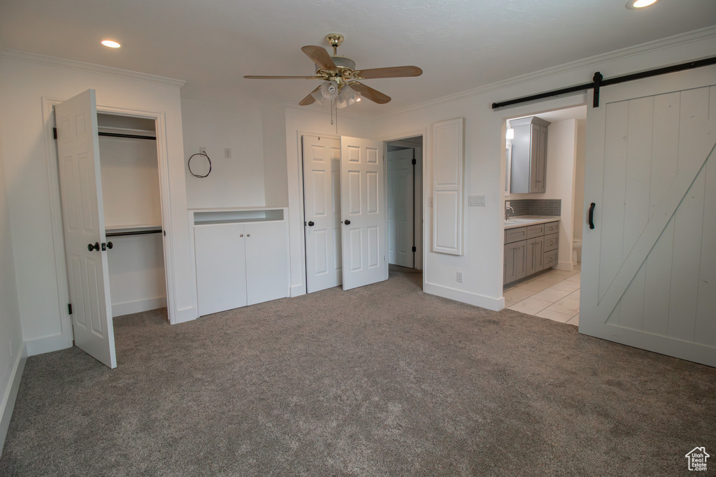 Unfurnished bedroom with ornamental molding, recessed lighting, light colored carpet, and a barn door
