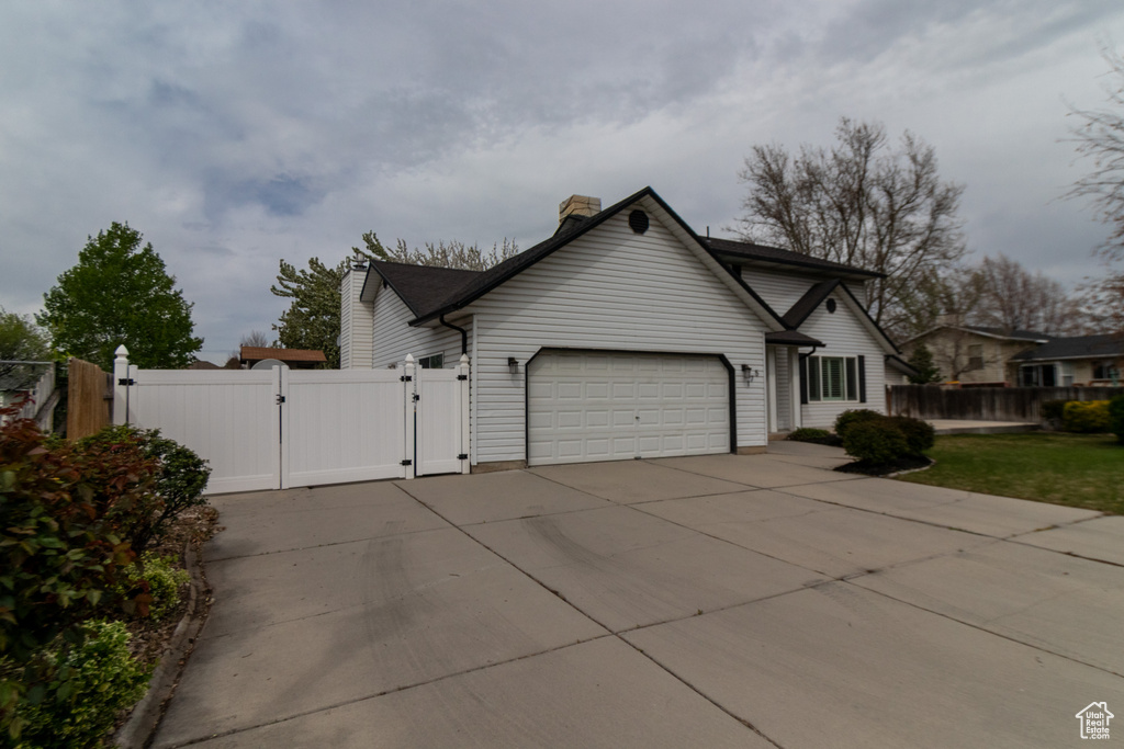View of front facade with a chimney, a gate, fence, an attached garage, and driveway