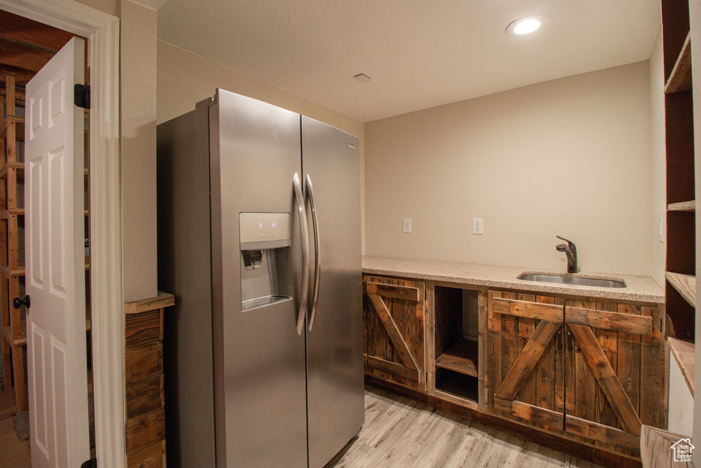 Kitchen featuring recessed lighting, light wood finished floors, a sink, light stone countertops, and stainless steel fridge