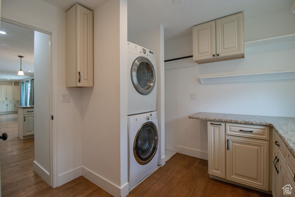 Clothes washing area with wood finished floors, stacked washer and dryer, baseboards, and laundry area