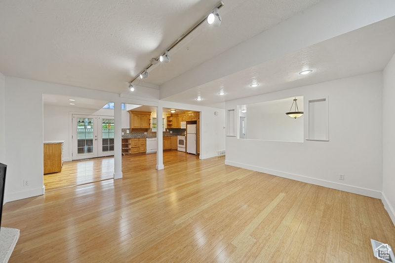 Unfurnished living room featuring light wood finished floors, baseboards, track lighting, and visible vents