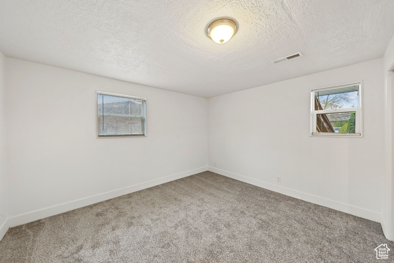 Empty room with baseboards, visible vents, carpet floors, and a textured ceiling
