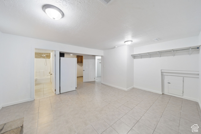 Finished below grade area featuring freestanding refrigerator, a textured ceiling, baseboards, and light tile patterned floors