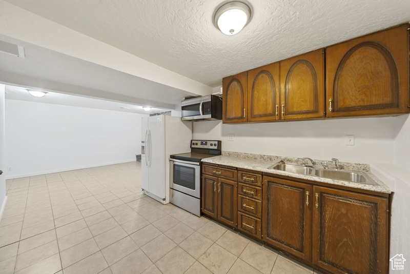 Kitchen featuring a sink, a textured ceiling, light tile patterned floors, light countertops, and appliances with stainless steel finishes