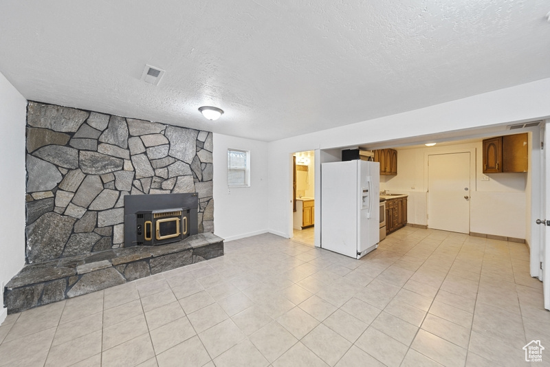 Unfurnished living room with a textured ceiling, light tile patterned flooring, baseboards, visible vents, and a wood stove