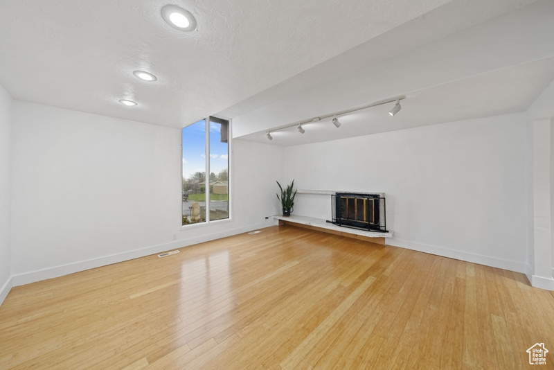 Unfurnished living room with recessed lighting, rail lighting, light wood-style floors, baseboards, and a glass covered fireplace