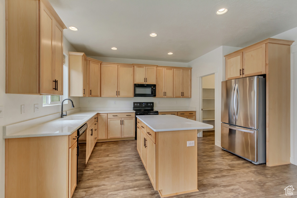 Kitchen featuring light wood finished floors, light brown cabinets, a sink, and black appliances