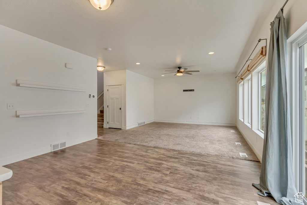 Unfurnished living room featuring wood finished floors, visible vents, baseboards, stairs, and ceiling fan