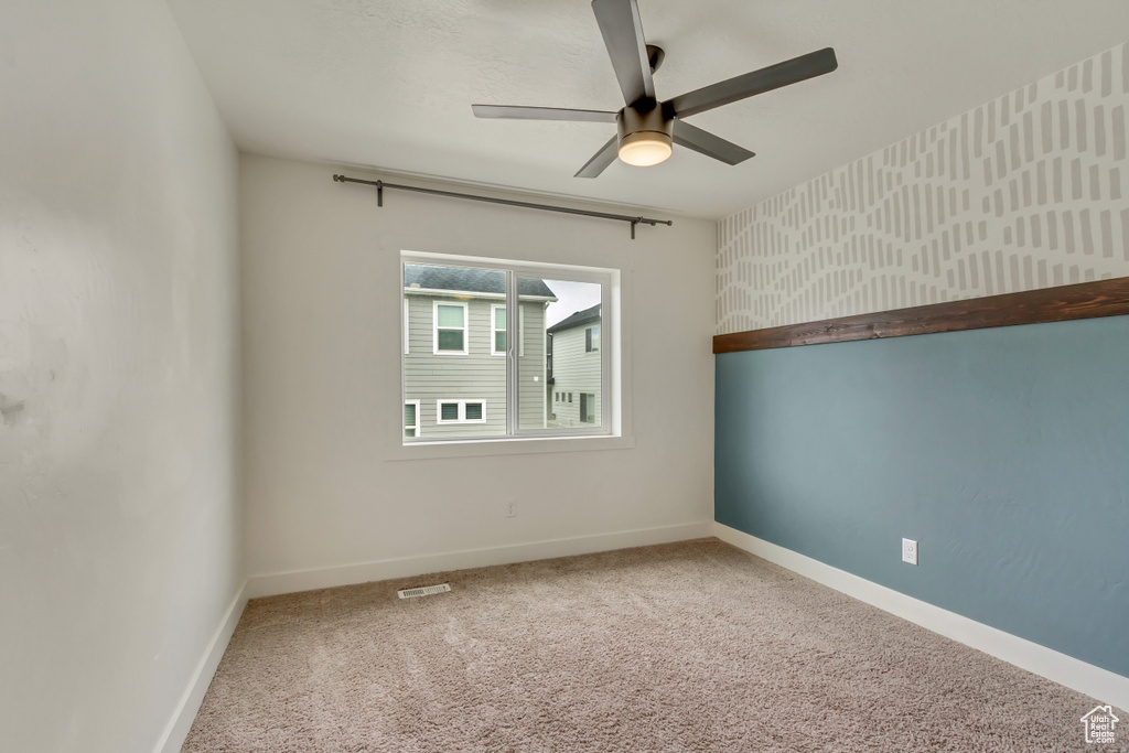 Spare room featuring carpet floors, visible vents, baseboards, and ceiling fan