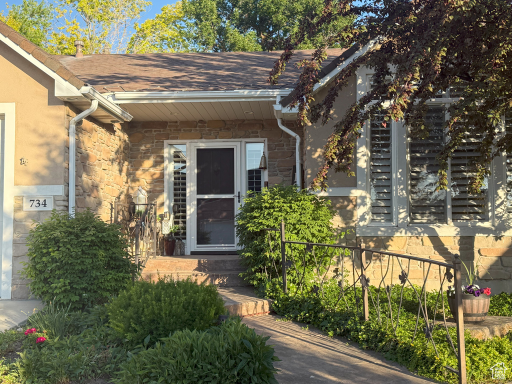 View of exterior entry featuring stone siding, roof with shingles, and stucco siding