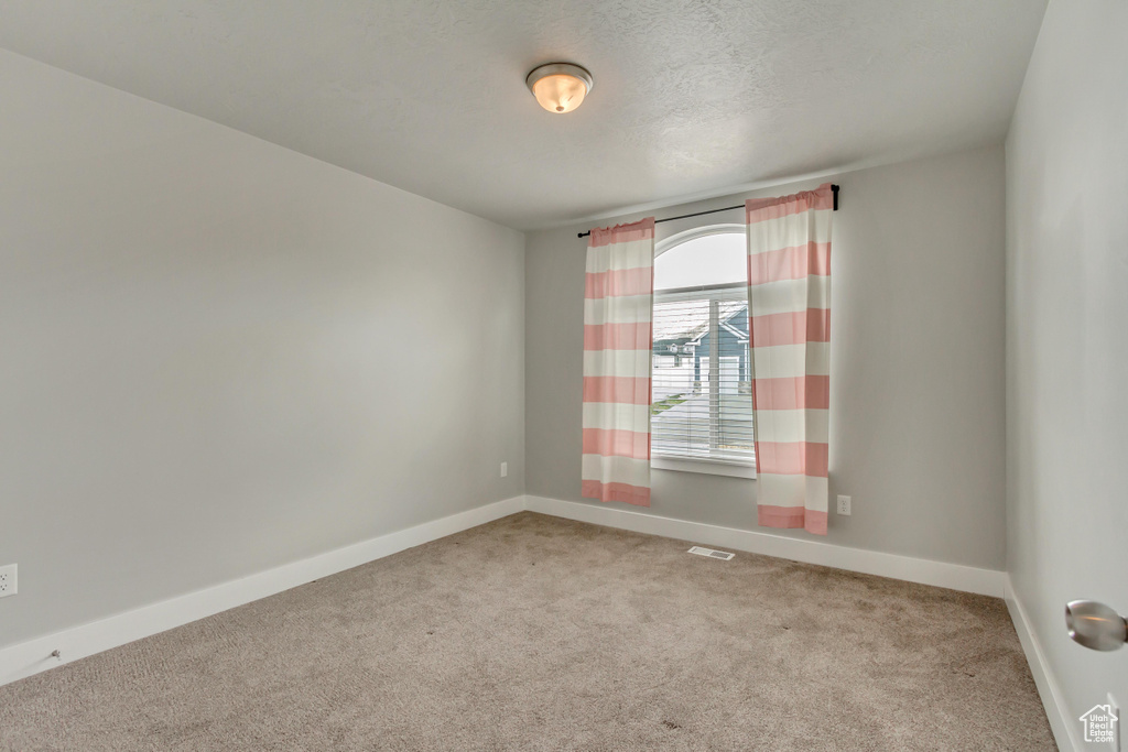 Carpeted empty room featuring a textured ceiling, visible vents, and baseboards