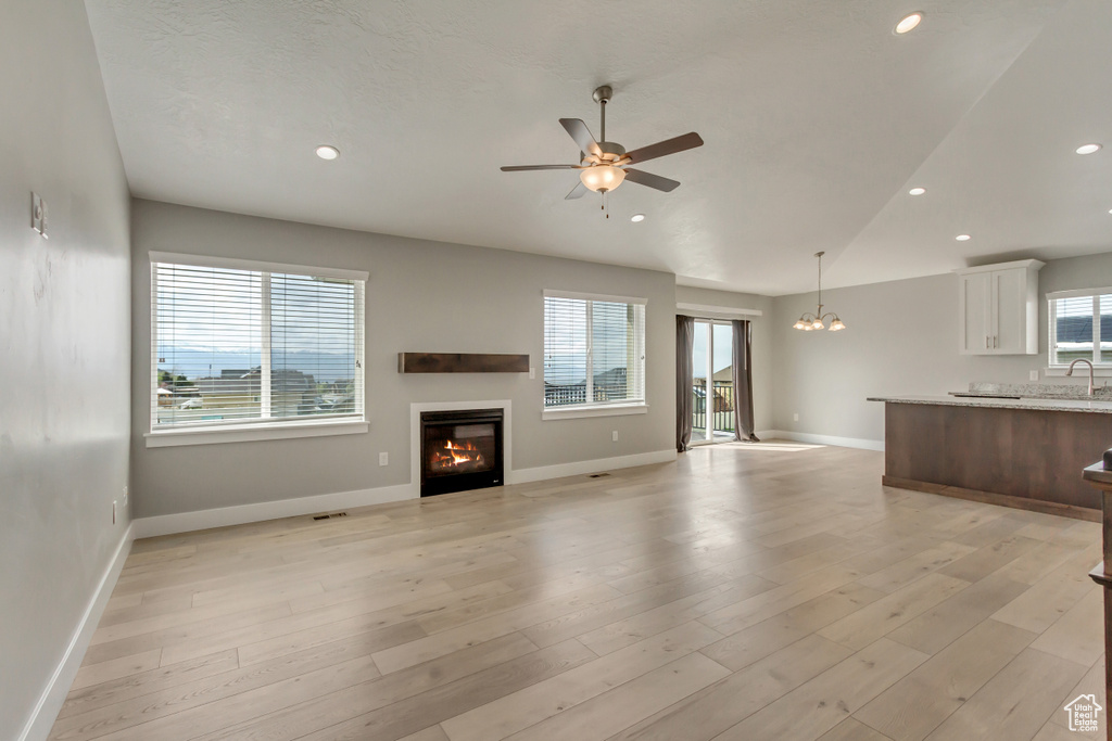 Unfurnished living room with a sink, ceiling fan with notable chandelier, a glass covered fireplace, light wood finished floors, and baseboards