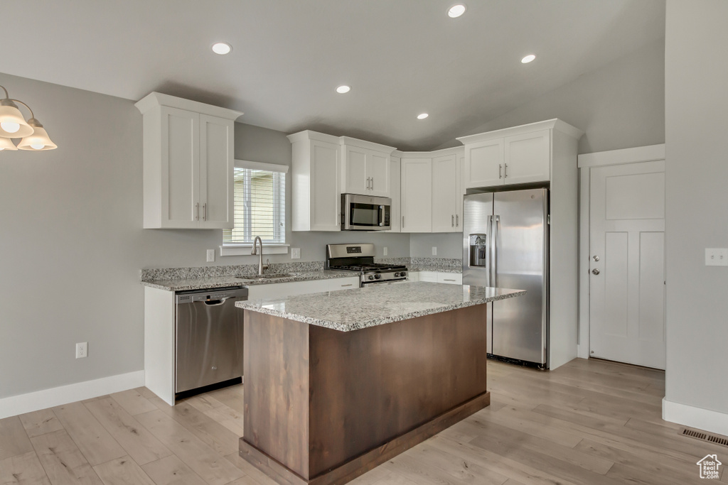 Kitchen featuring a center island, a sink, stainless steel appliances, light wood-style flooring, and white cabinetry