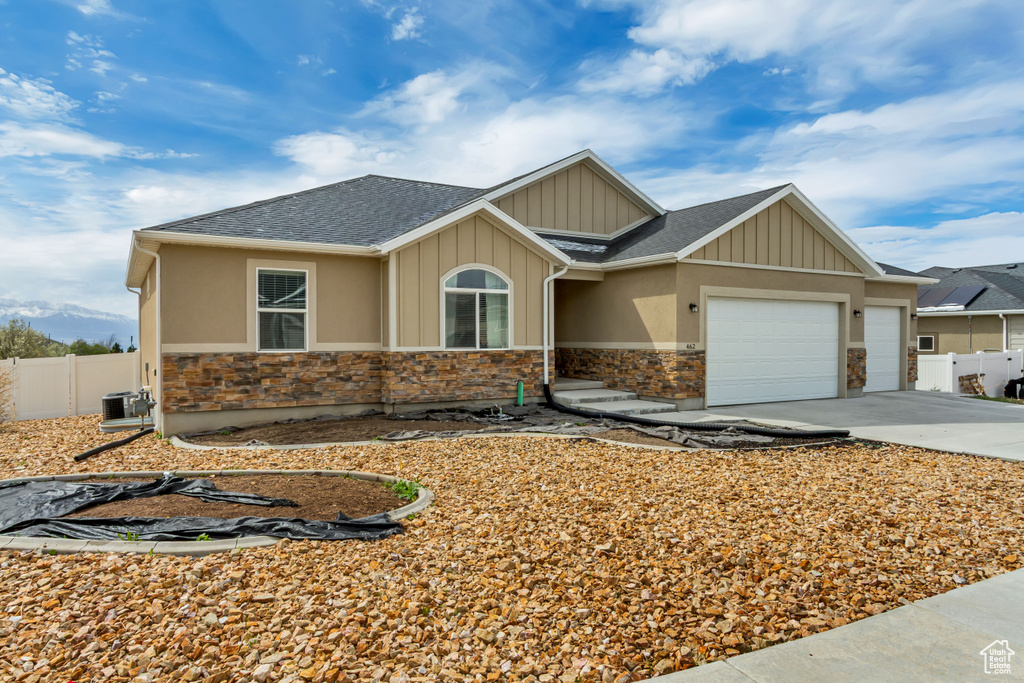 View of front facade with concrete driveway, fence, stone siding, and a garage