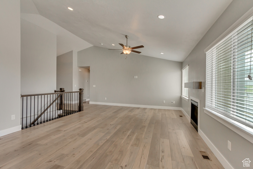 Unfurnished living room featuring ceiling fan, lofted ceiling, visible vents, and light wood-style flooring