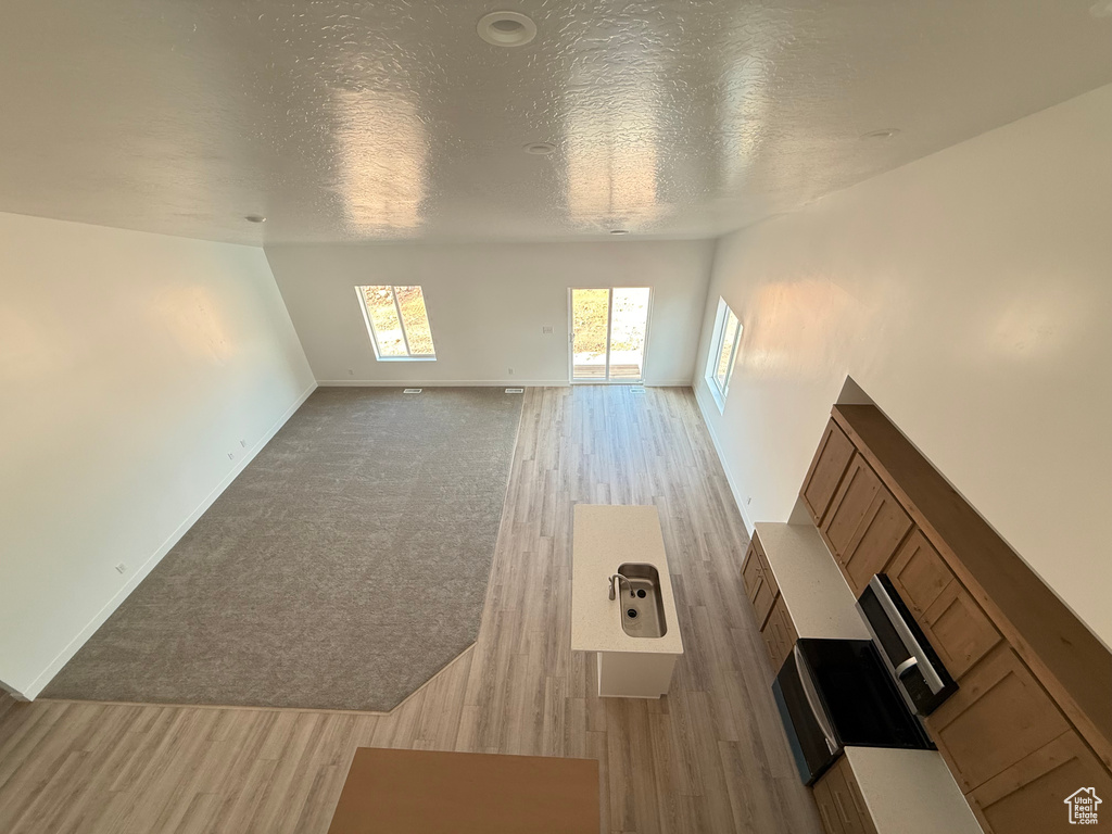 Unfurnished living room with light wood-style floors, a textured ceiling, and baseboards