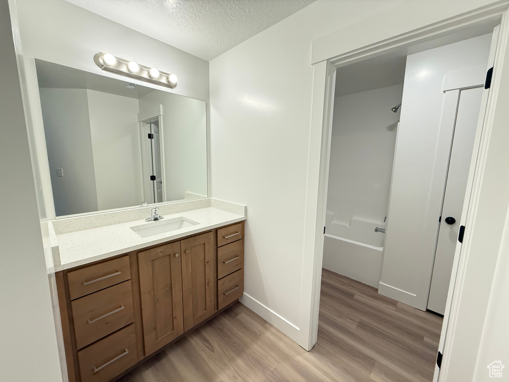 Full bathroom featuring wood finished floors, vanity, shower / washtub combination, a textured ceiling, and baseboards