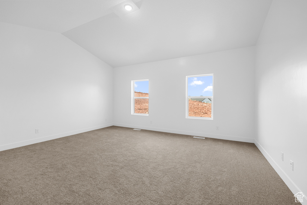 Carpeted spare room featuring lofted ceiling and baseboards